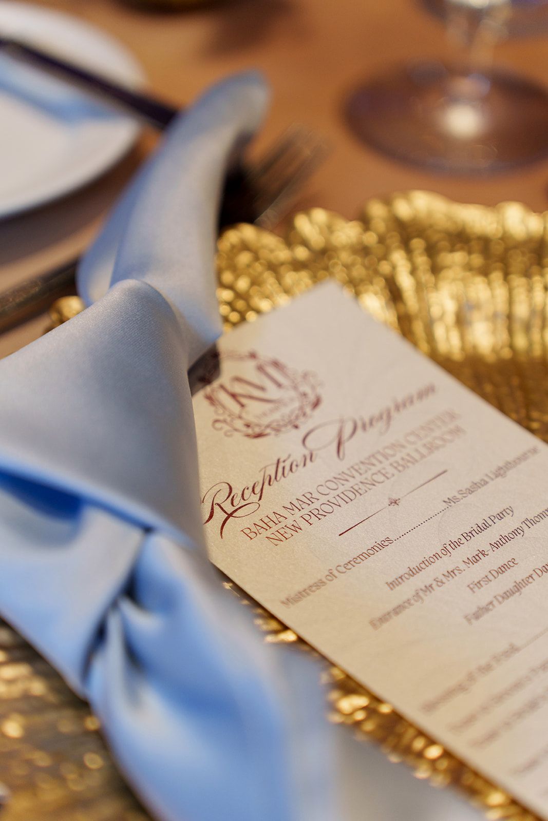 Wedding reception program tucked in a blue satin napkin on a gold sequin tablescape setting.