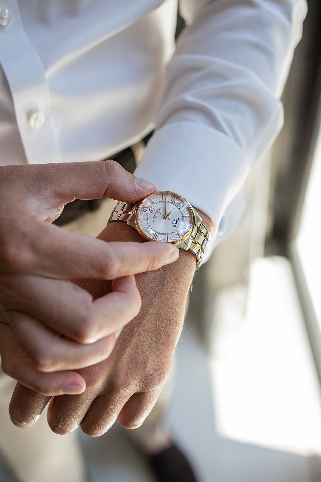 Man in white dress shirt adjusting a two-tone gold and silver luxury wristwatch on his wrist.