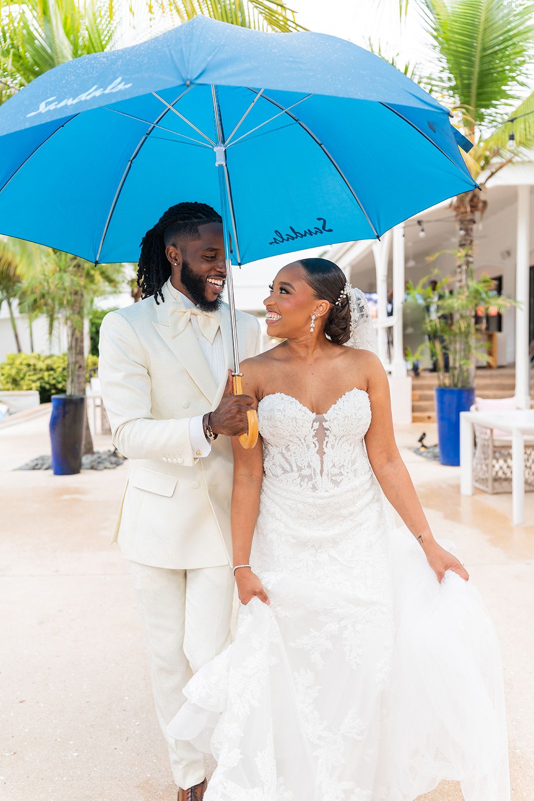 A joyful bride and groom share a romantic moment under a blue Sandals umbrella at a tropical resort wedding.