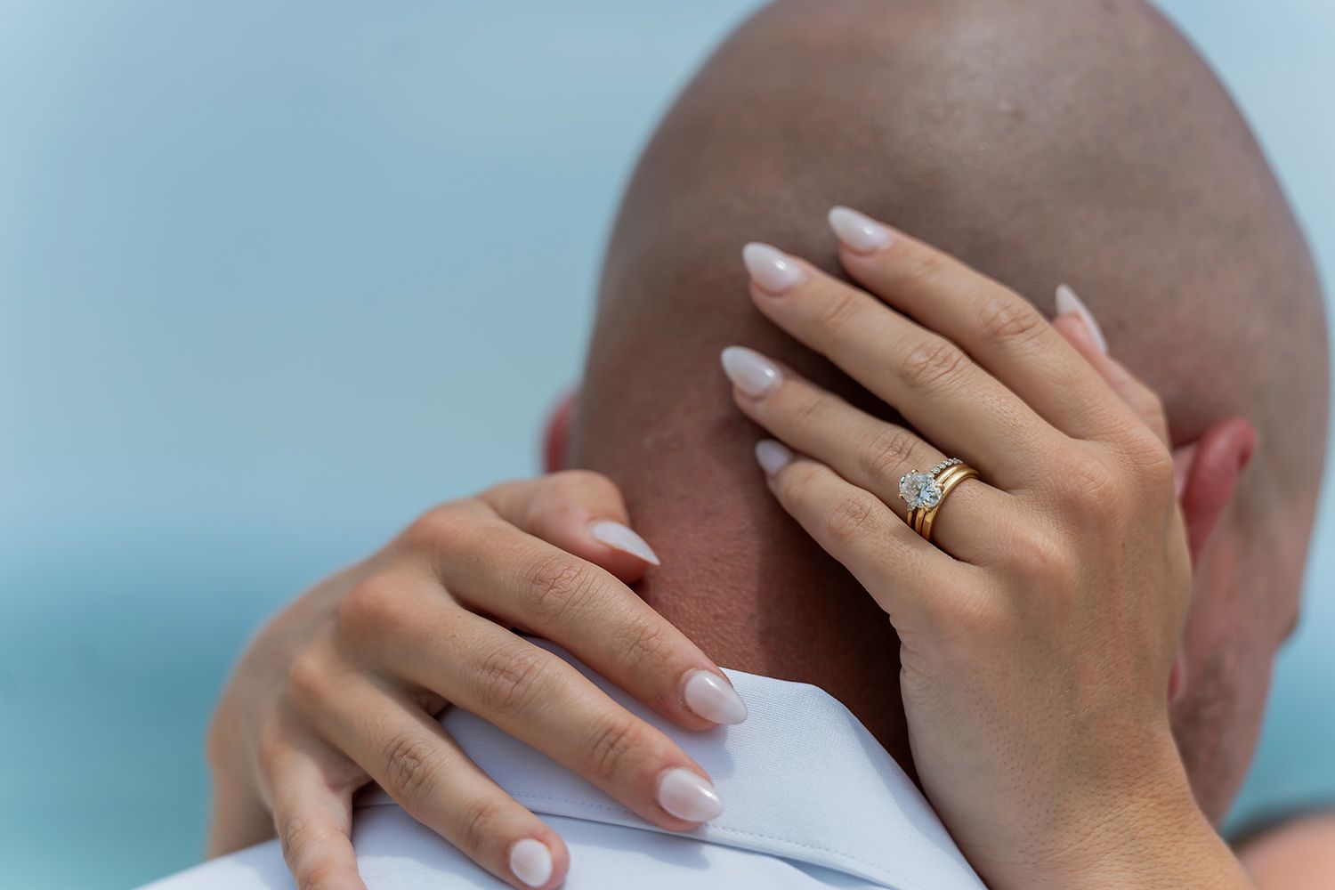 Close-up of a woman's hand with French manicure and gold diamond ring resting on a bald man's shoulder.