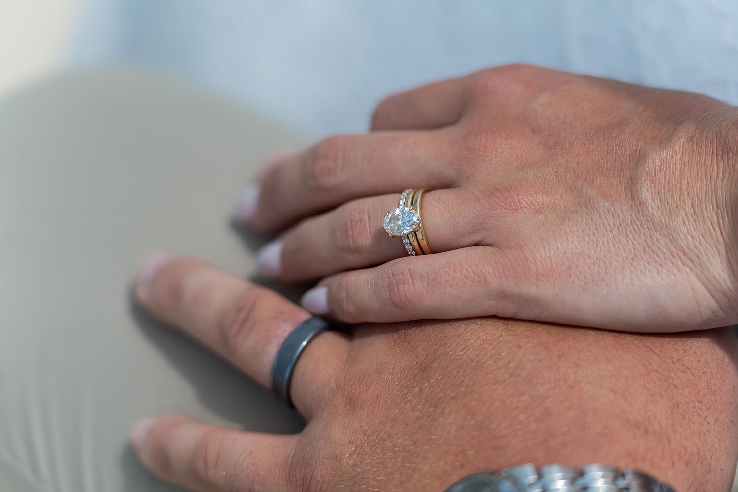 Close-up of couple's hands showing diamond engagement ring and gold wedding band with black silicone ring.