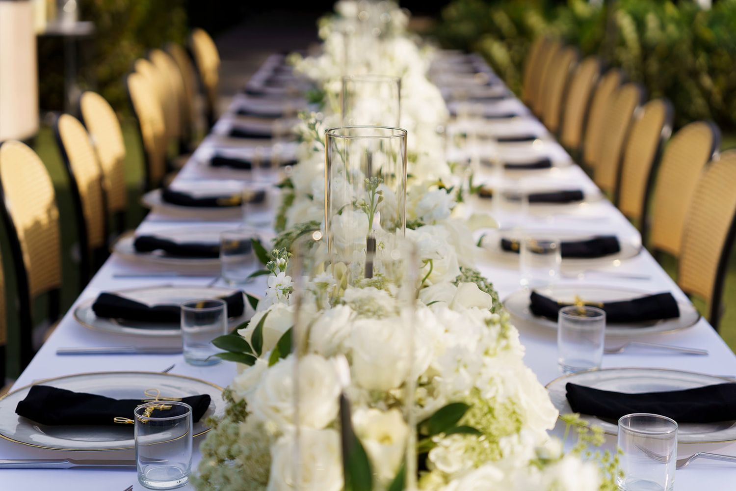 Elegant long banquet table with white floral centerpieces, black napkins, and glassware for a formal wedding reception.