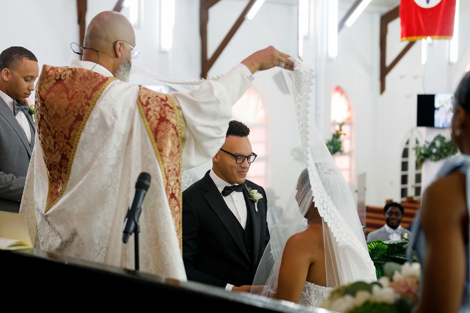 Priest lifting veil over bride and groom during traditional church wedding ceremony.