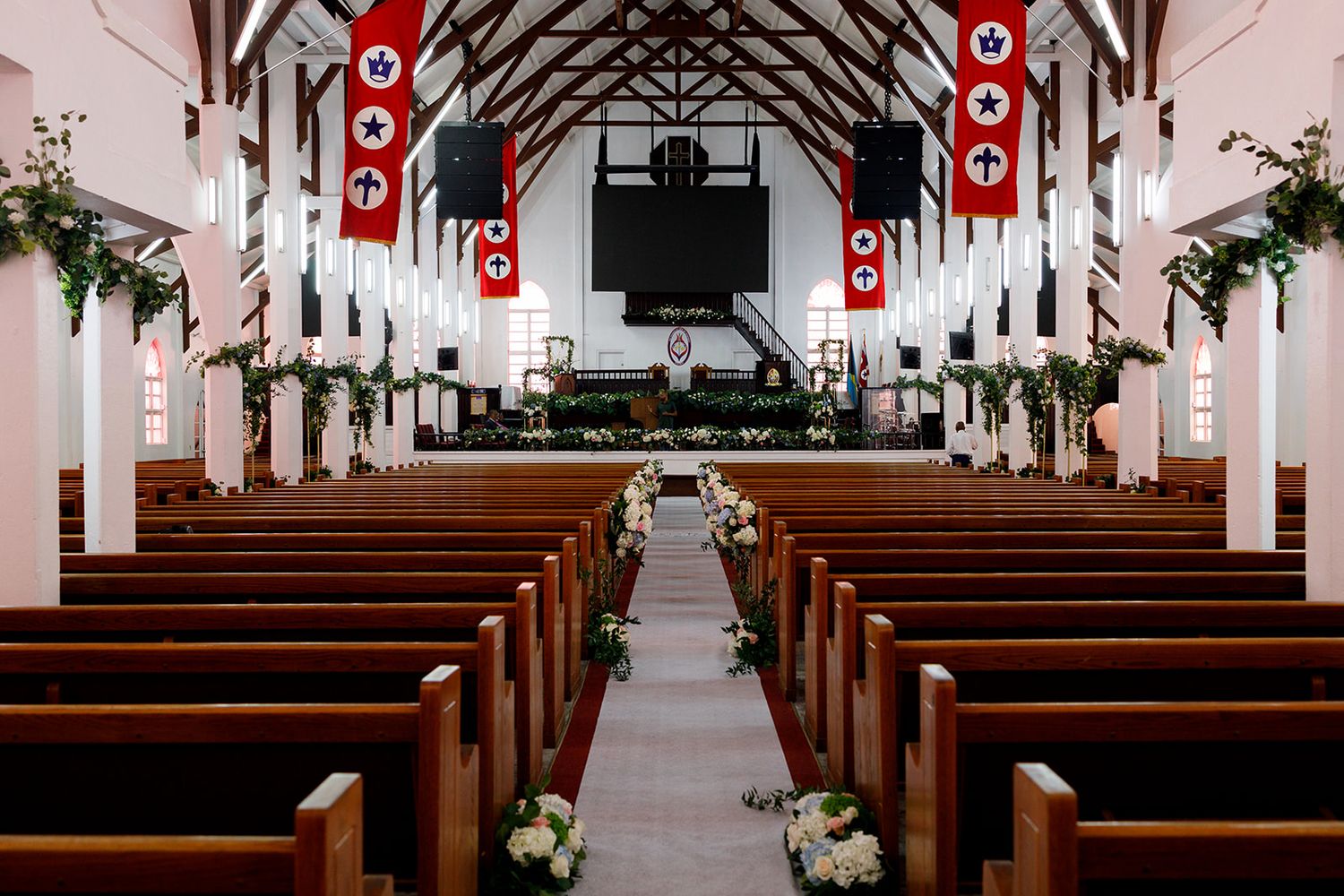 Elegant church wedding venue with wooden pews, floral arrangements, and red banners lining the aisle.