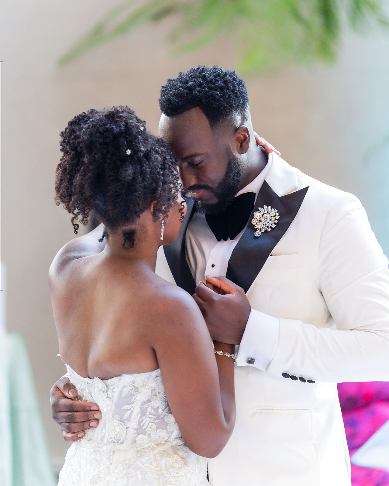 A bride and groom share an intimate moment, dressed in wedding attire, with the groom in a white tuxedo and black bow tie.