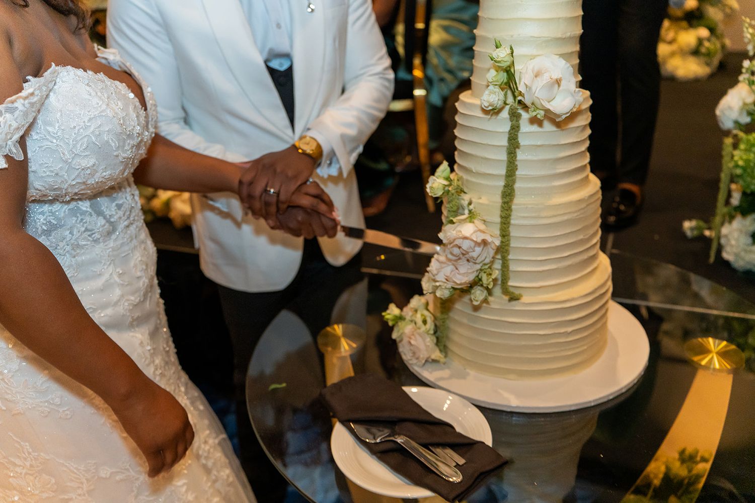 Bride and groom cutting elegant white multi-tiered wedding cake adorned with fresh flowers.