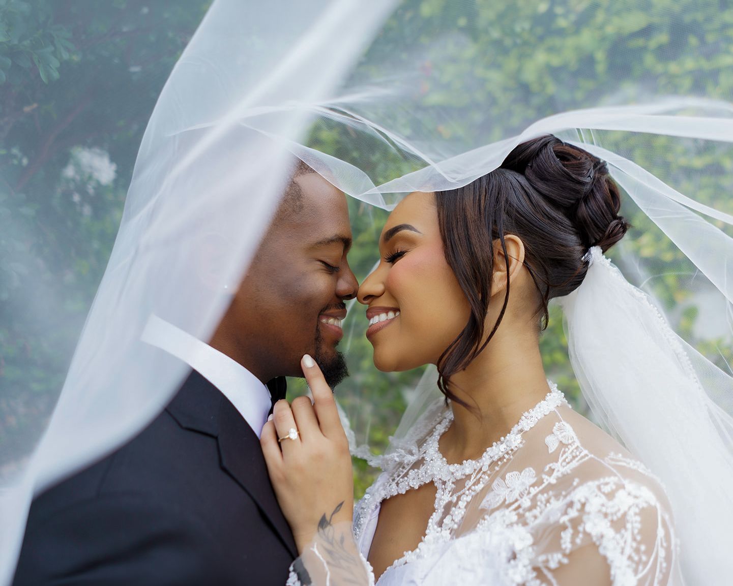 A bride and groom share a romantic moment under a flowing white veil on their wedding day.