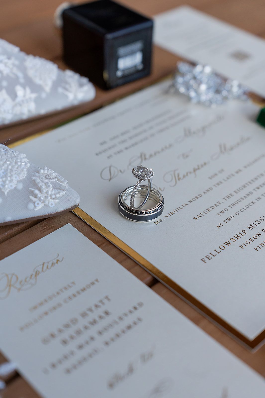 Elegant wedding stationery with gold script, diamond engagement ring, and wedding bands displayed on wooden surface.