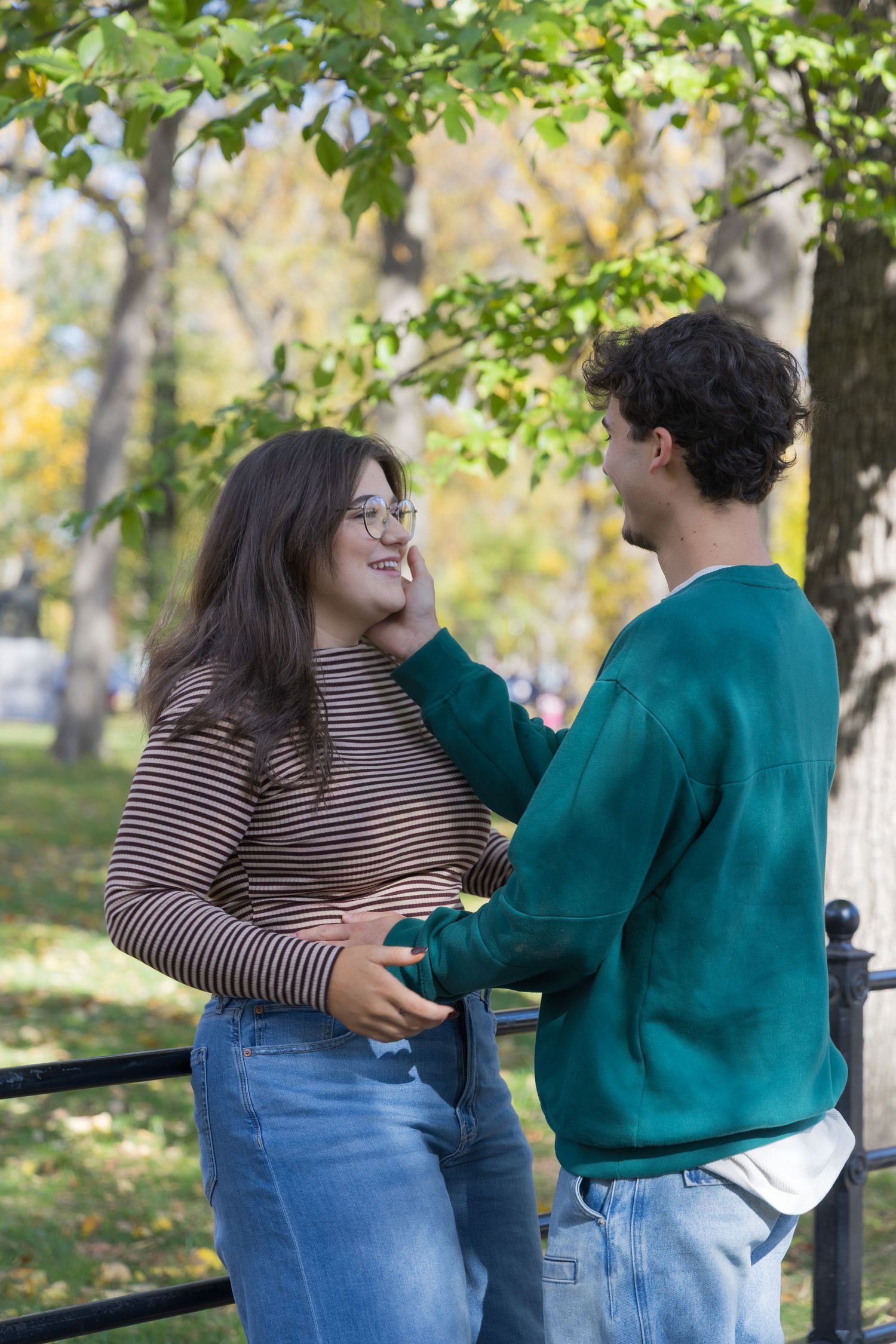 A couple in casual clothing share an intimate moment while standing together in a park on an autumn day.