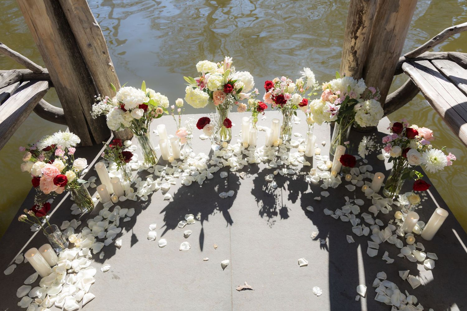 Elegant wedding ceremony floral arrangement with white and red roses, petals scattered on a dock overlooking water.