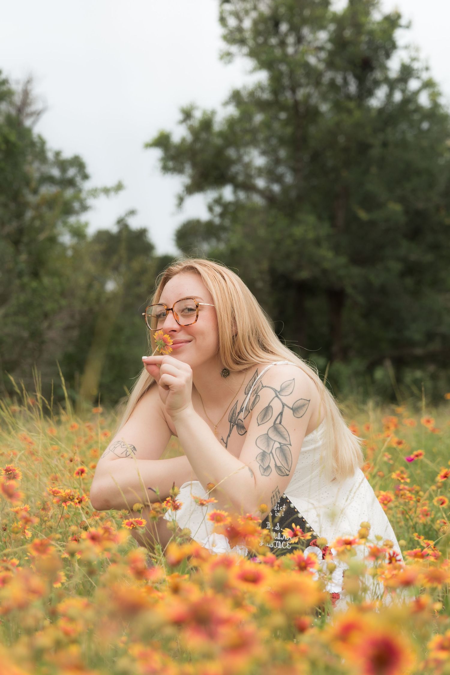 Smiling blonde woman with arm tattoo lying in a vibrant orange wildflower field.