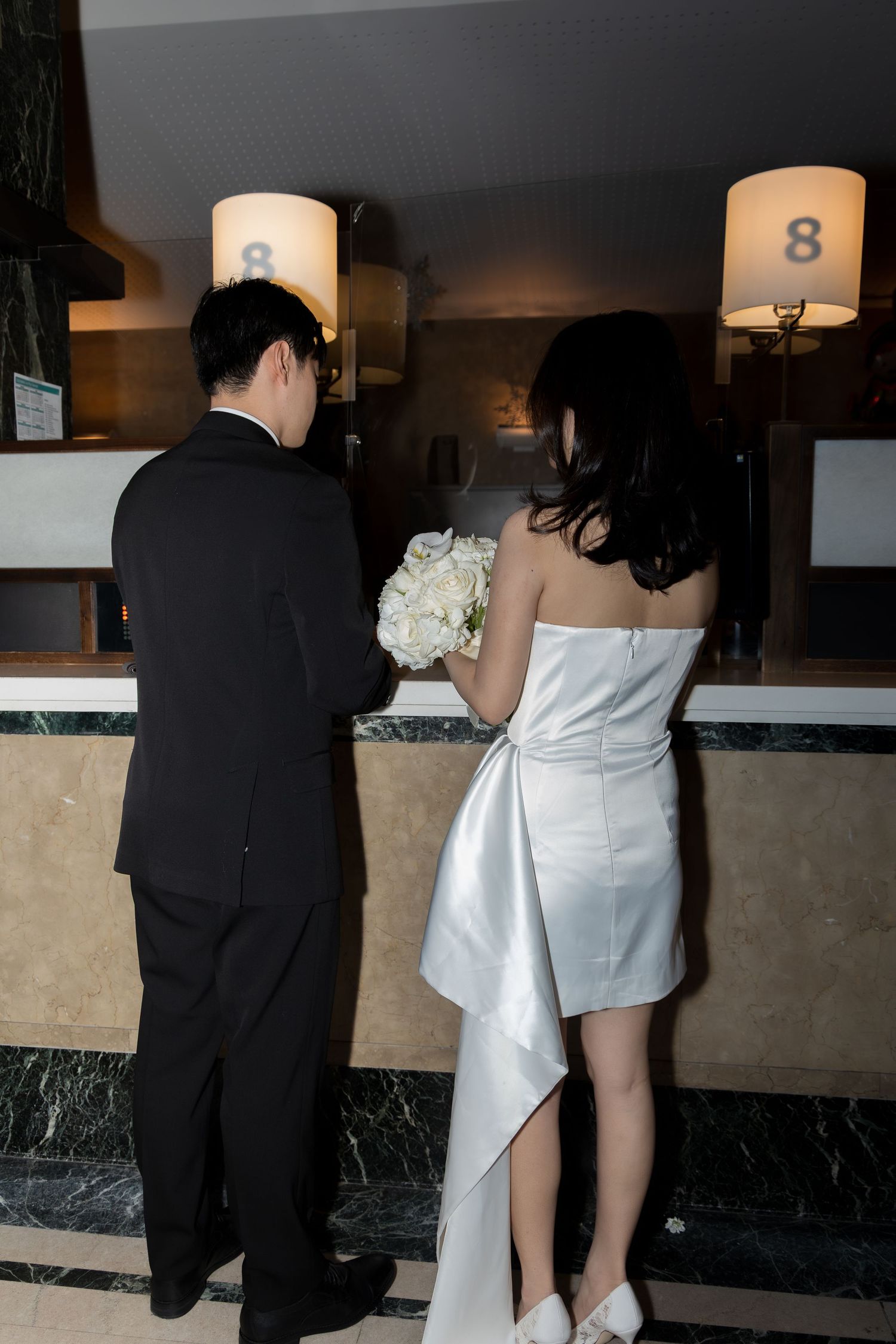 Couple signing their marriage license at the glass window counter of the City Clerk's office with a witness present