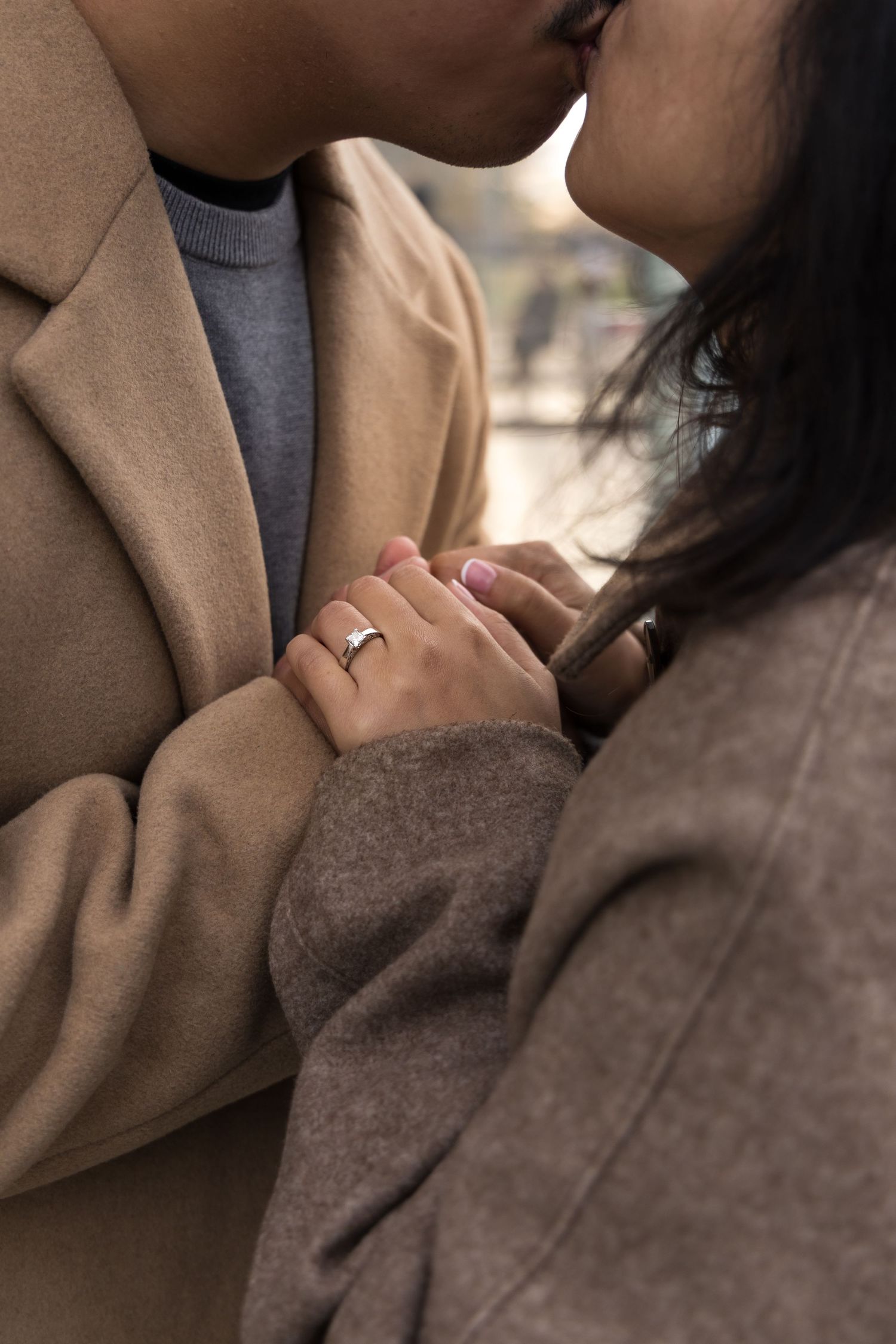 A romantic close-up of clasped hands with a wedding ring, wearing cozy winter coats in brown and gray tones.