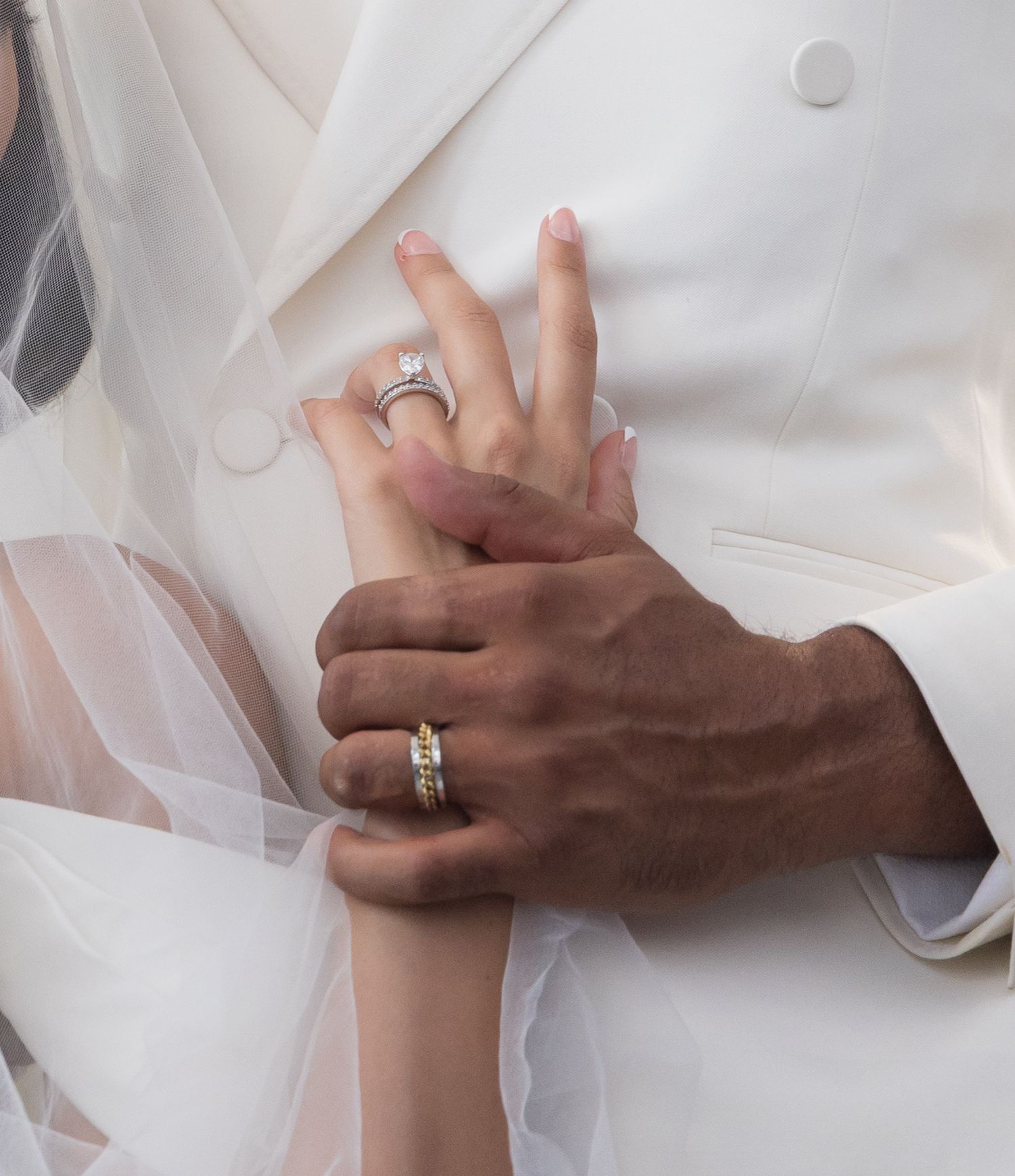 Two hands with wedding rings intertwined against a white fabric background, showing an intimate moment between partners.