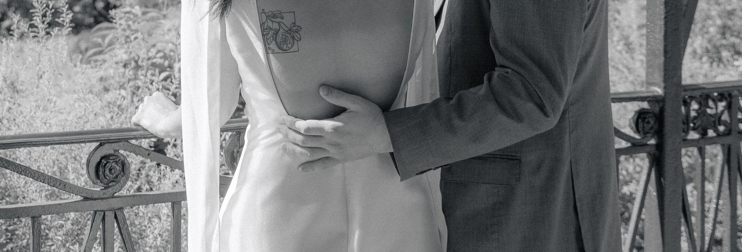 Black and white photo of a couple embracing at their wedding, bride in white gown and groom in gray suit.