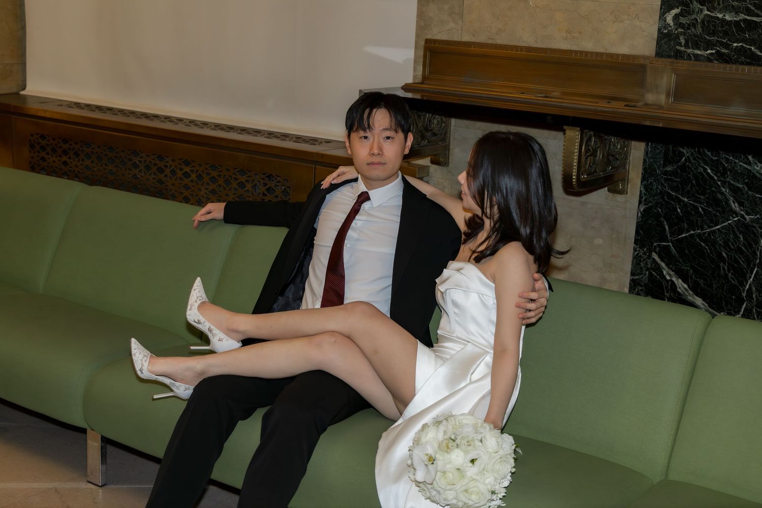 A couple shares a romantic moment while sitting on a green couch in the NYC Marriage Bureau
