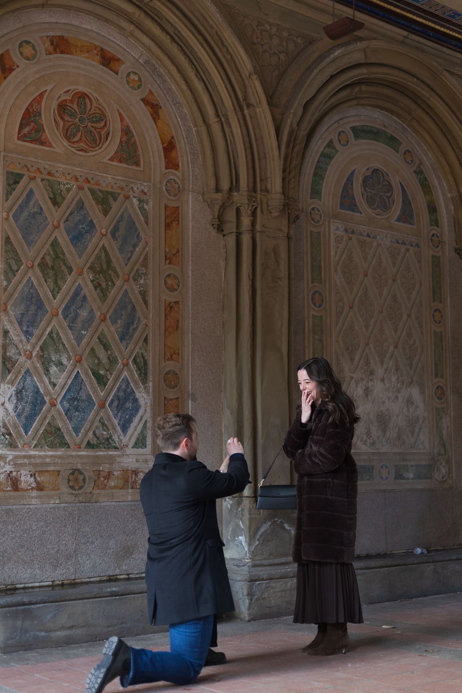 Man proposes on one knee to woman at Bethesda Terrace in Central Park, NYC.