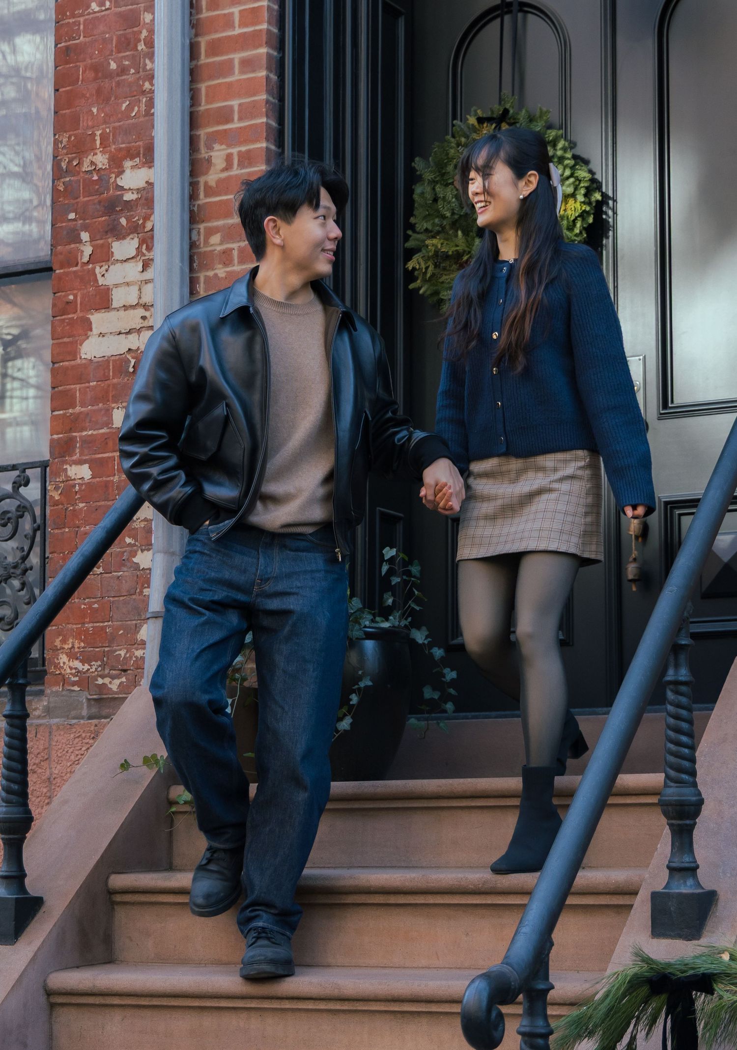 Couple holding hands on brownstone steps in fall outfits, smiling at each other in an urban setting.