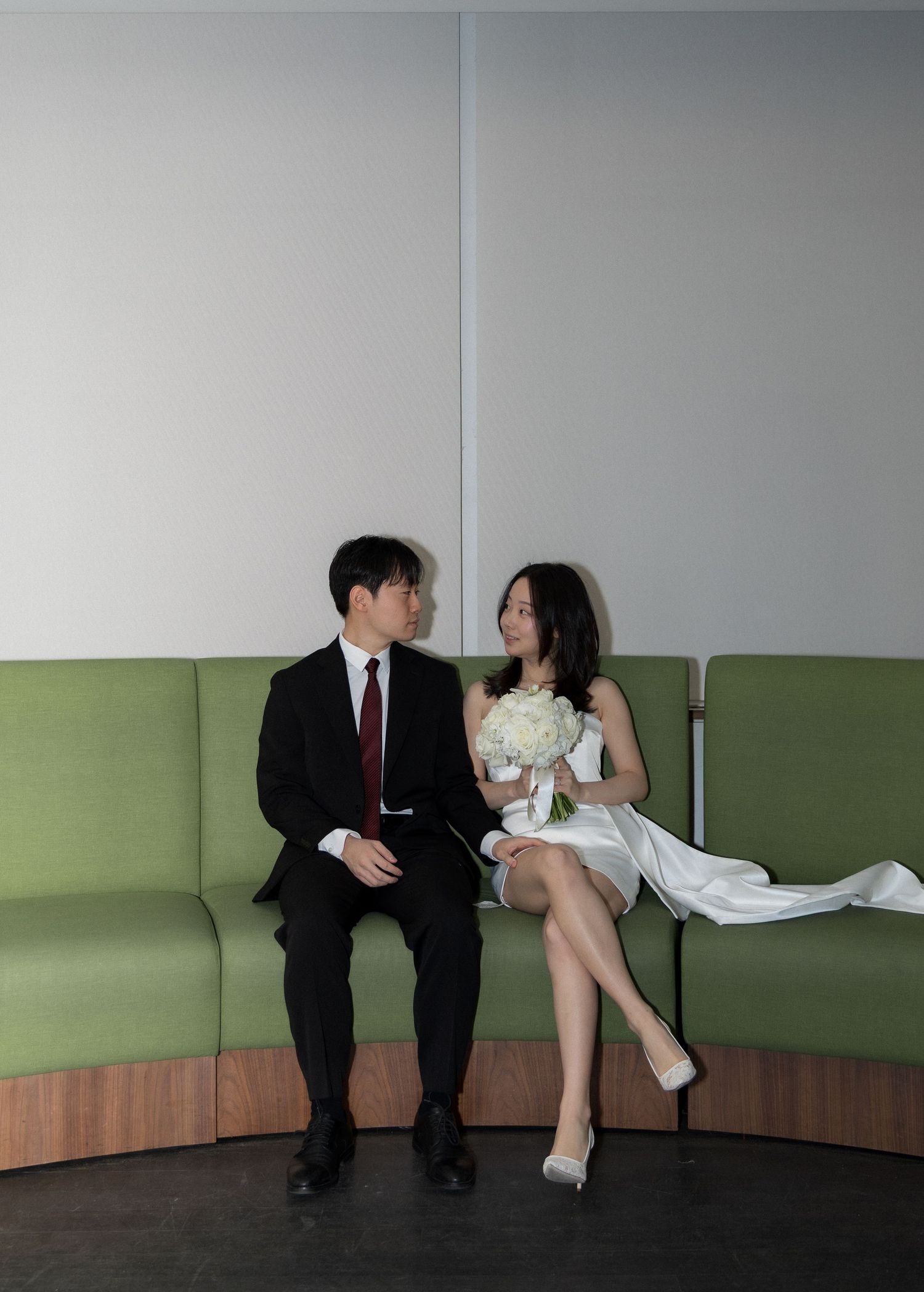A couple sits together on a green couch in a minimalist room, sharing a romantic moment.