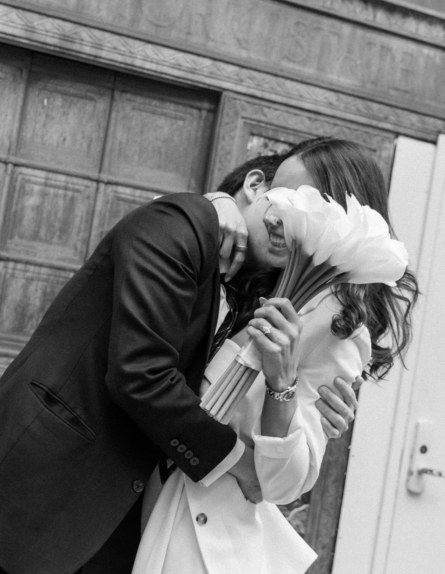 A black and white photo showing a couple in wedding attire sharing romantic dips and kisses outdoors.