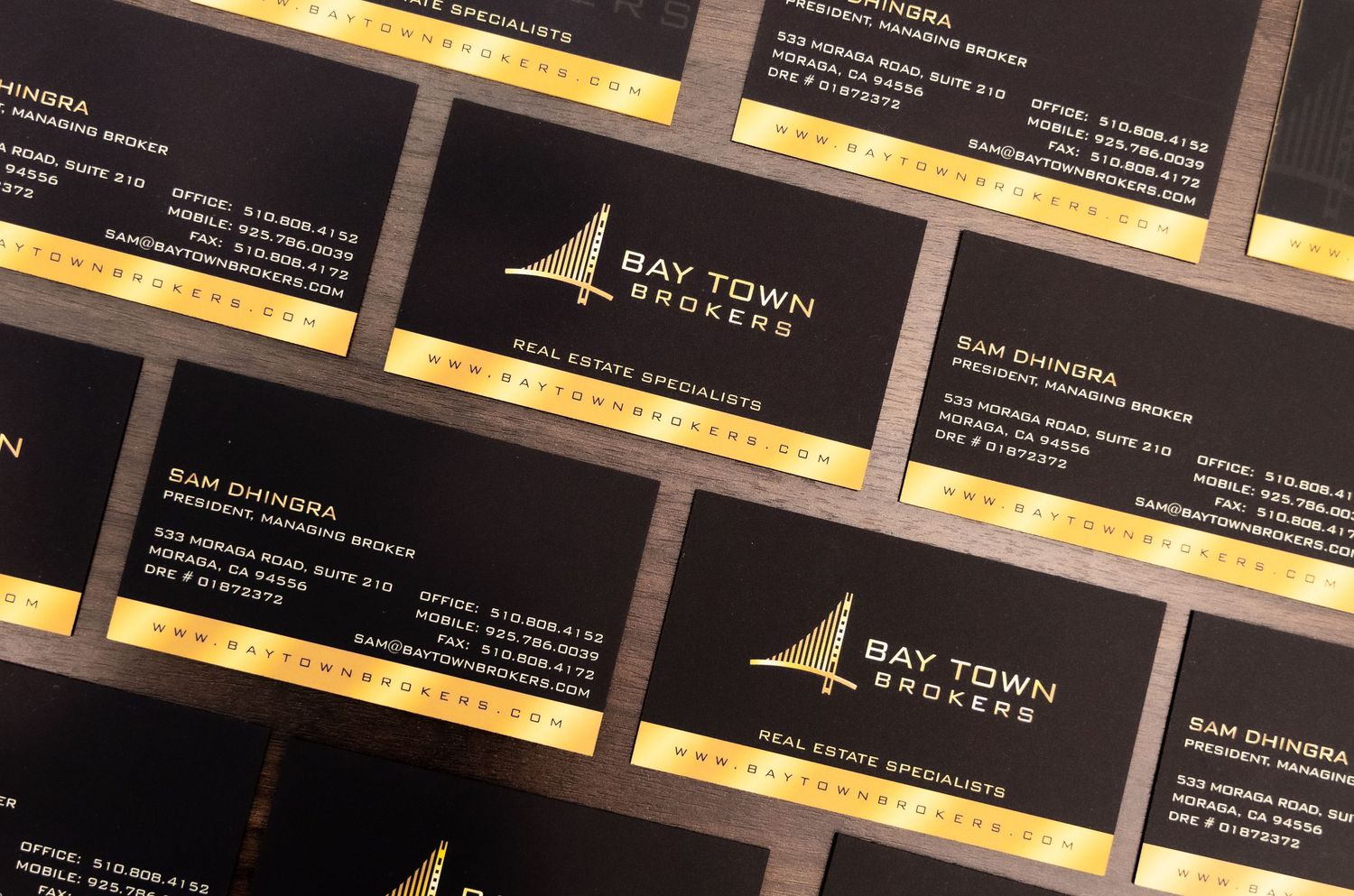 Rows of black and gold business cards for Bay Town Brokers arranged in a diagonal pattern.