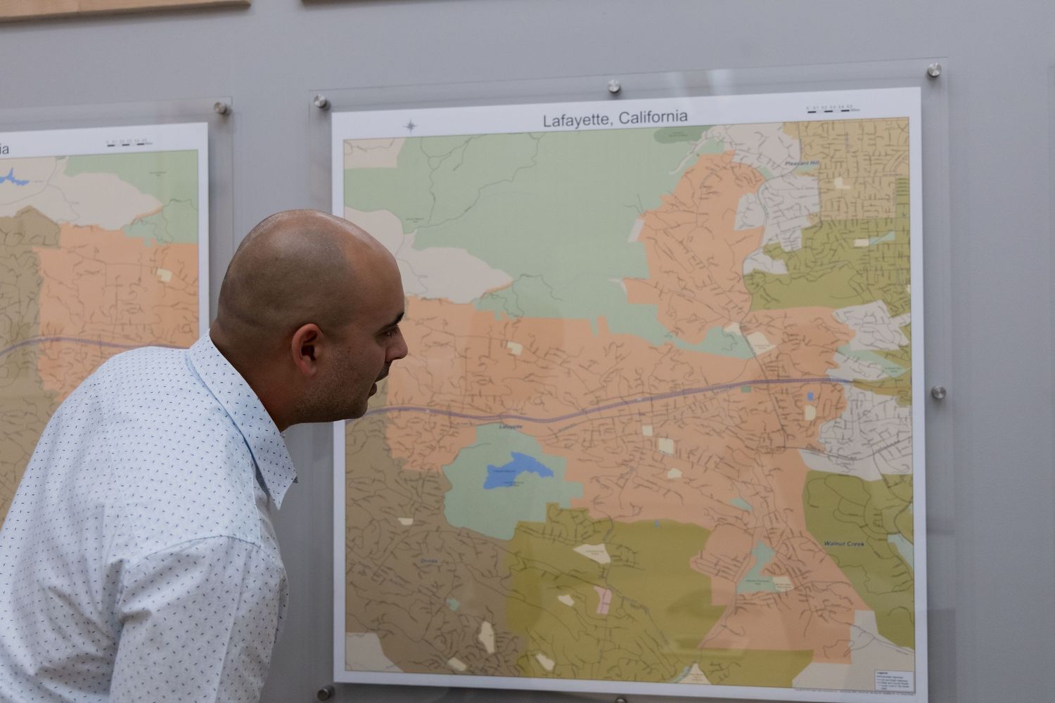 A person examines a large wall-mounted map showing geographic regions and boundaries.