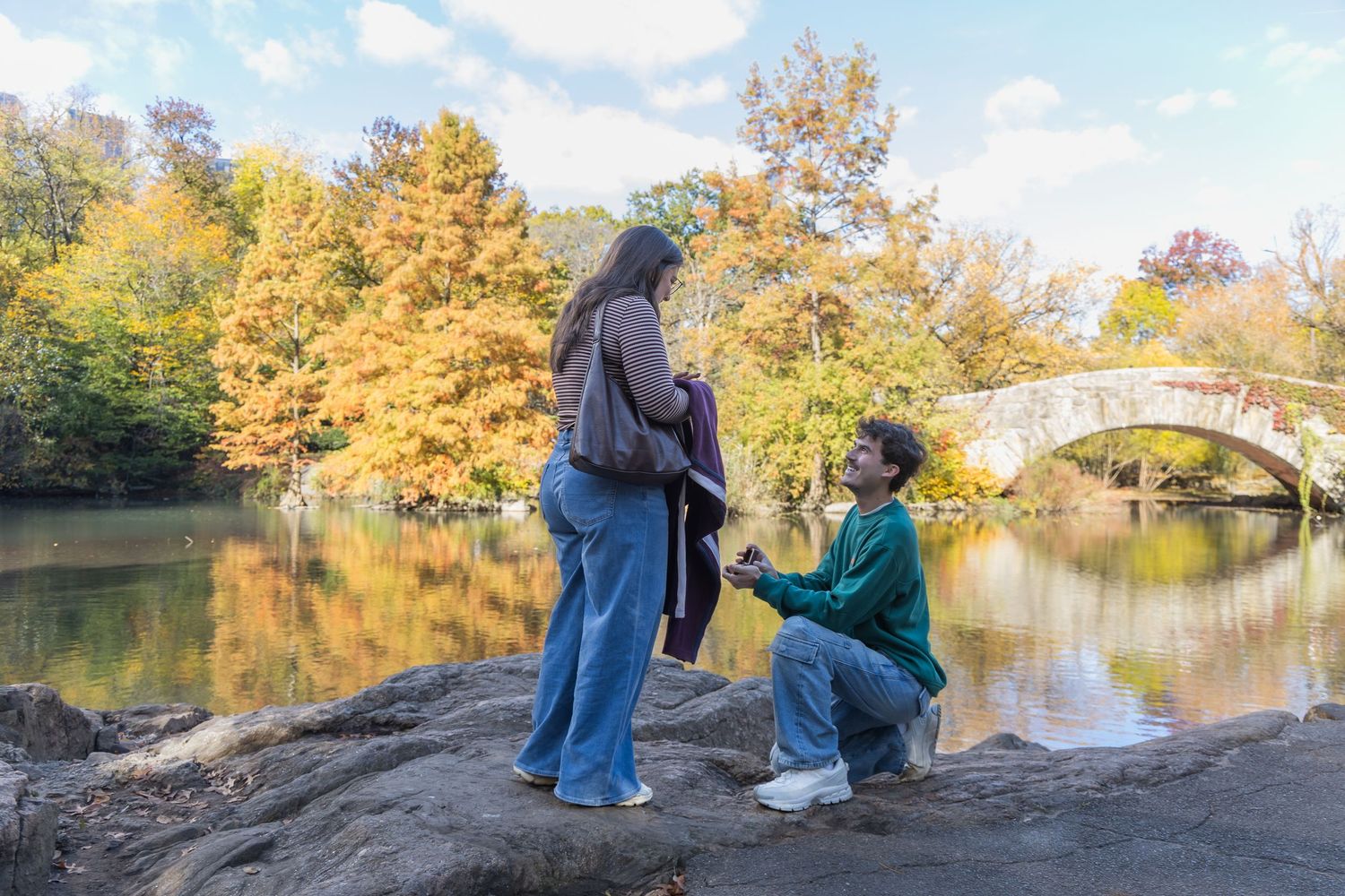 Man proposing on one knee in front of Gapstow Bridge in Central Park