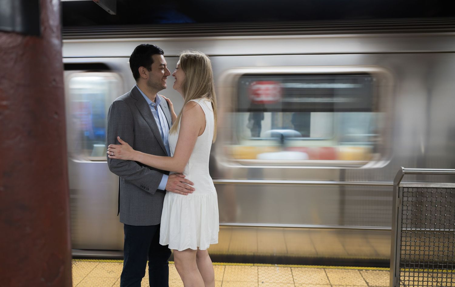Couple kissing romantically in a subway station with a blurred train passing behind them.