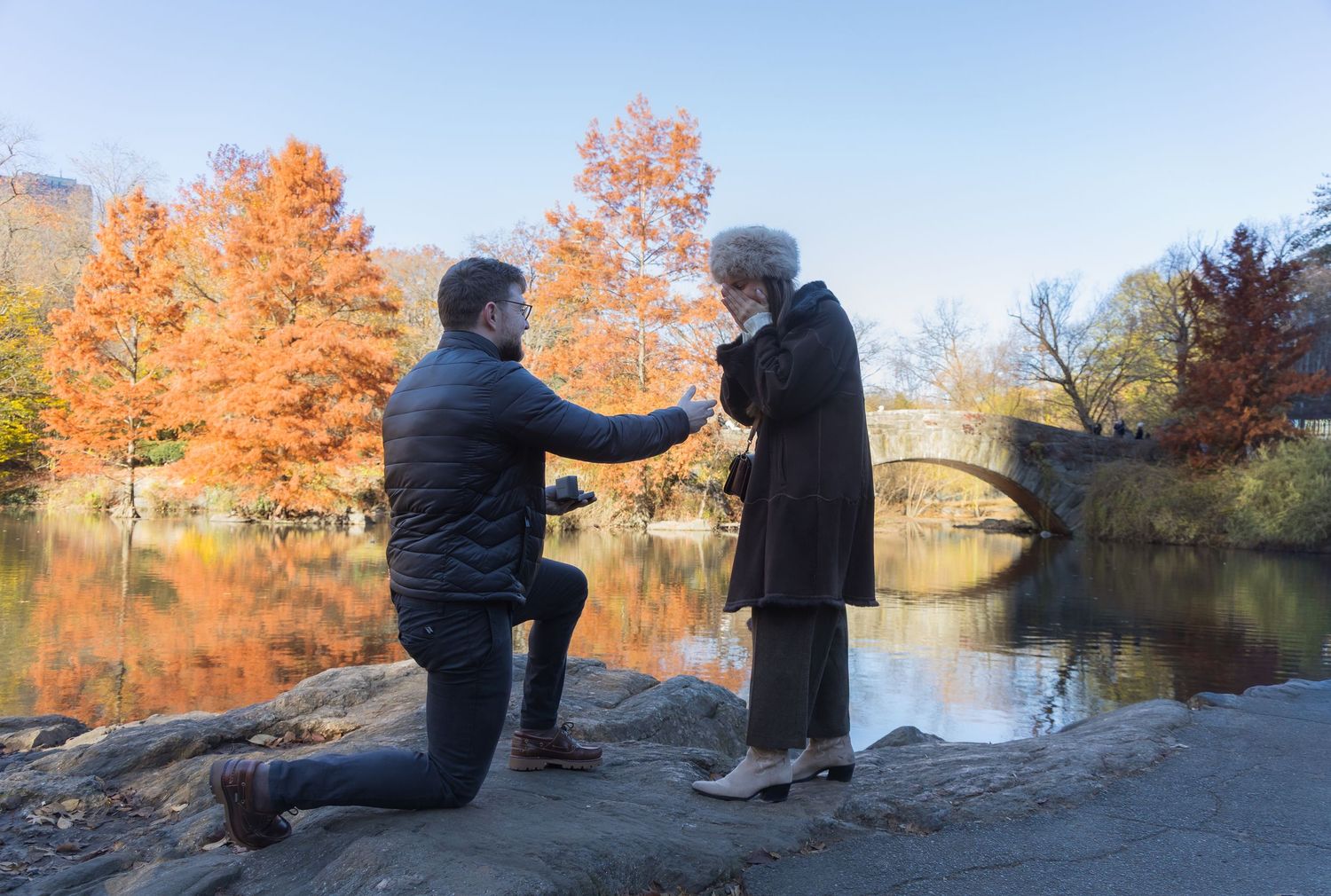 Man proposing to his girlfriend in front of Gapstow Bridge in Central Park in the fall