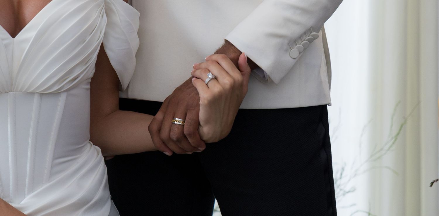 A person in a white dress shirt and black pants stands against a white wall in a professional setting.