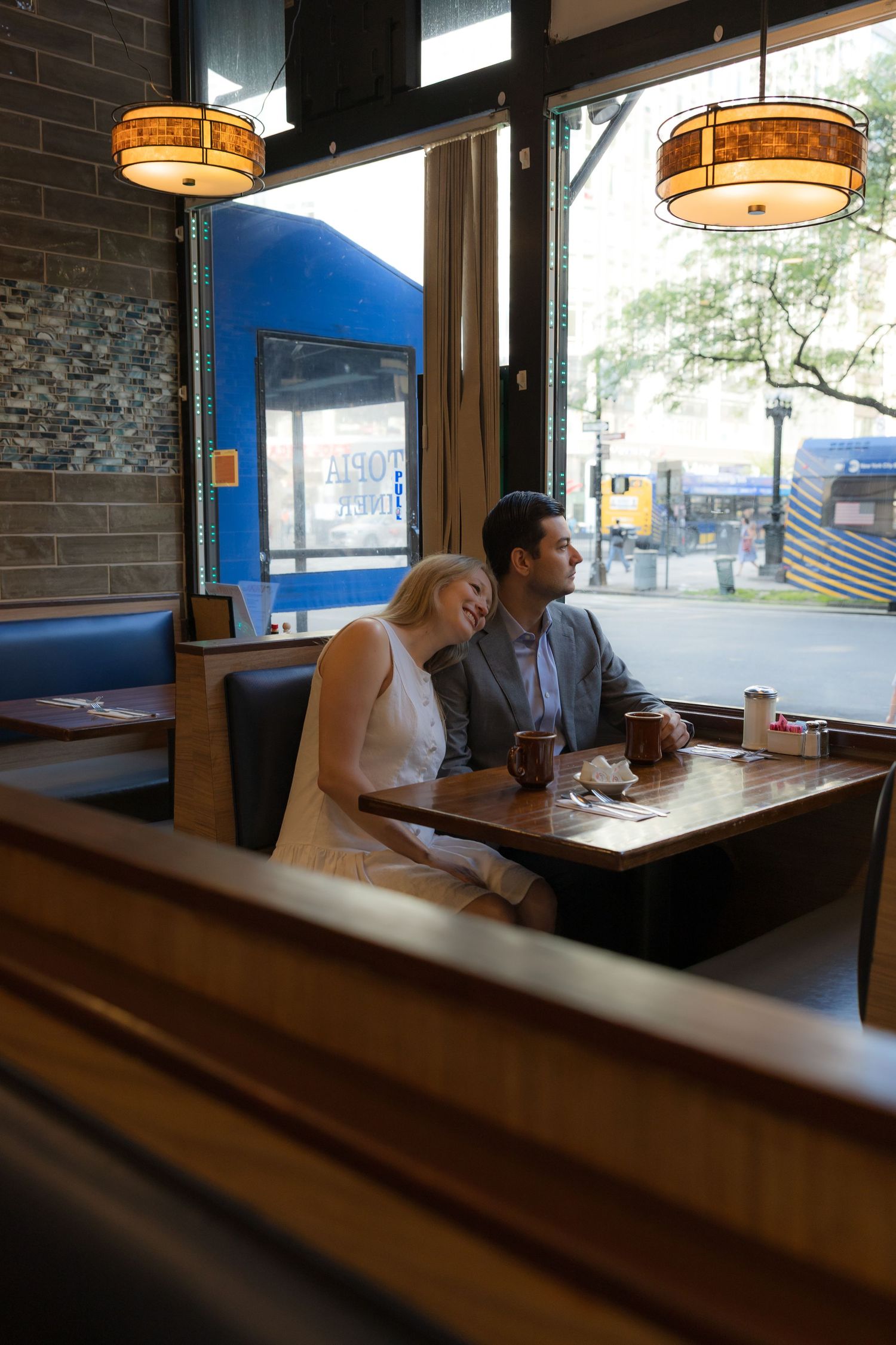 Couple sitting close together in a cozy diner booth by the window, sharing a romantic moment over drinks.