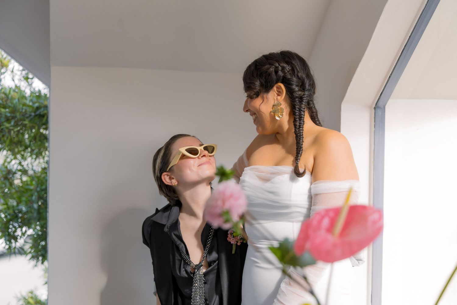 Two people share a joyful moment together while holding pink flowers in a bright indoor setting.