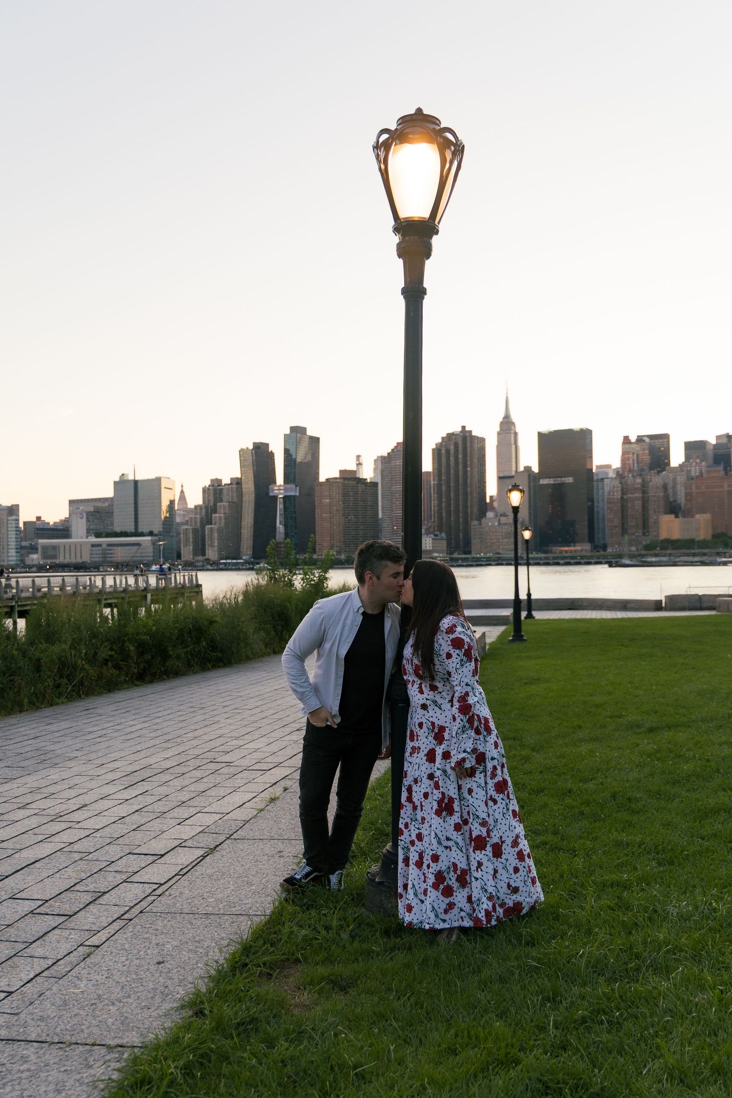Couple kissing under a glowing street lamp at dusk with NYC skyline and Empire State Building in background.