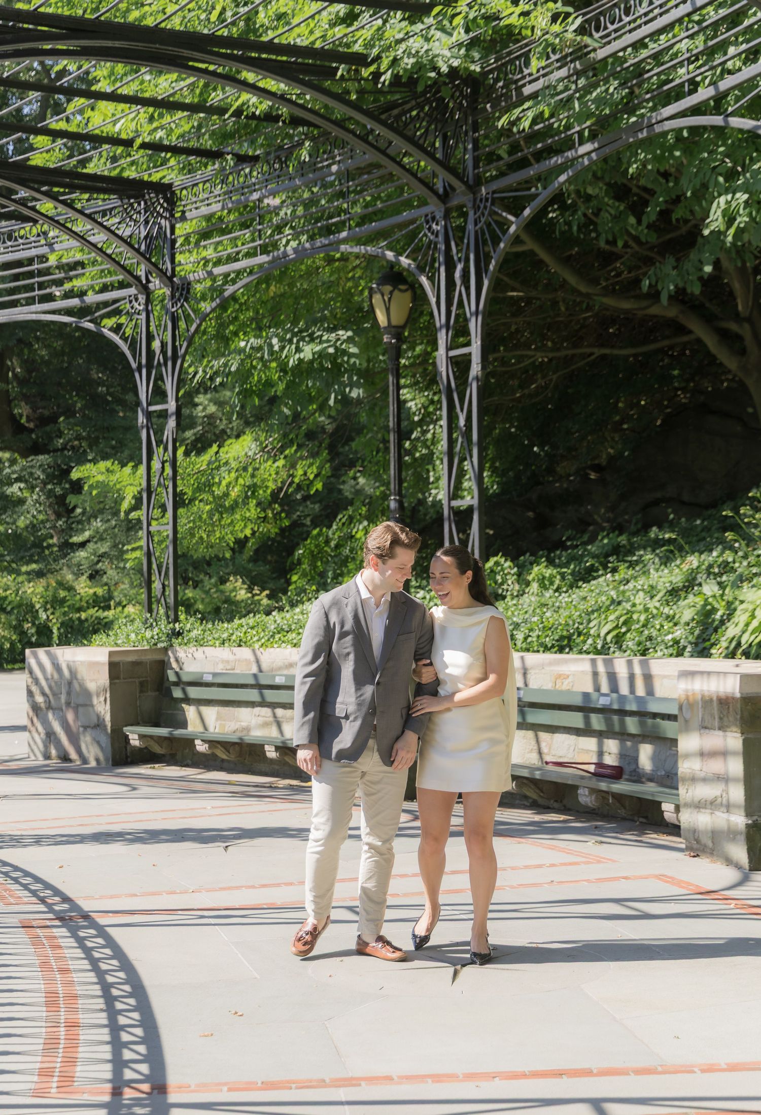 A couple walking hand-in-hand beneath the wisteria pergola during their Conservatory Garden engagement session in Central Park