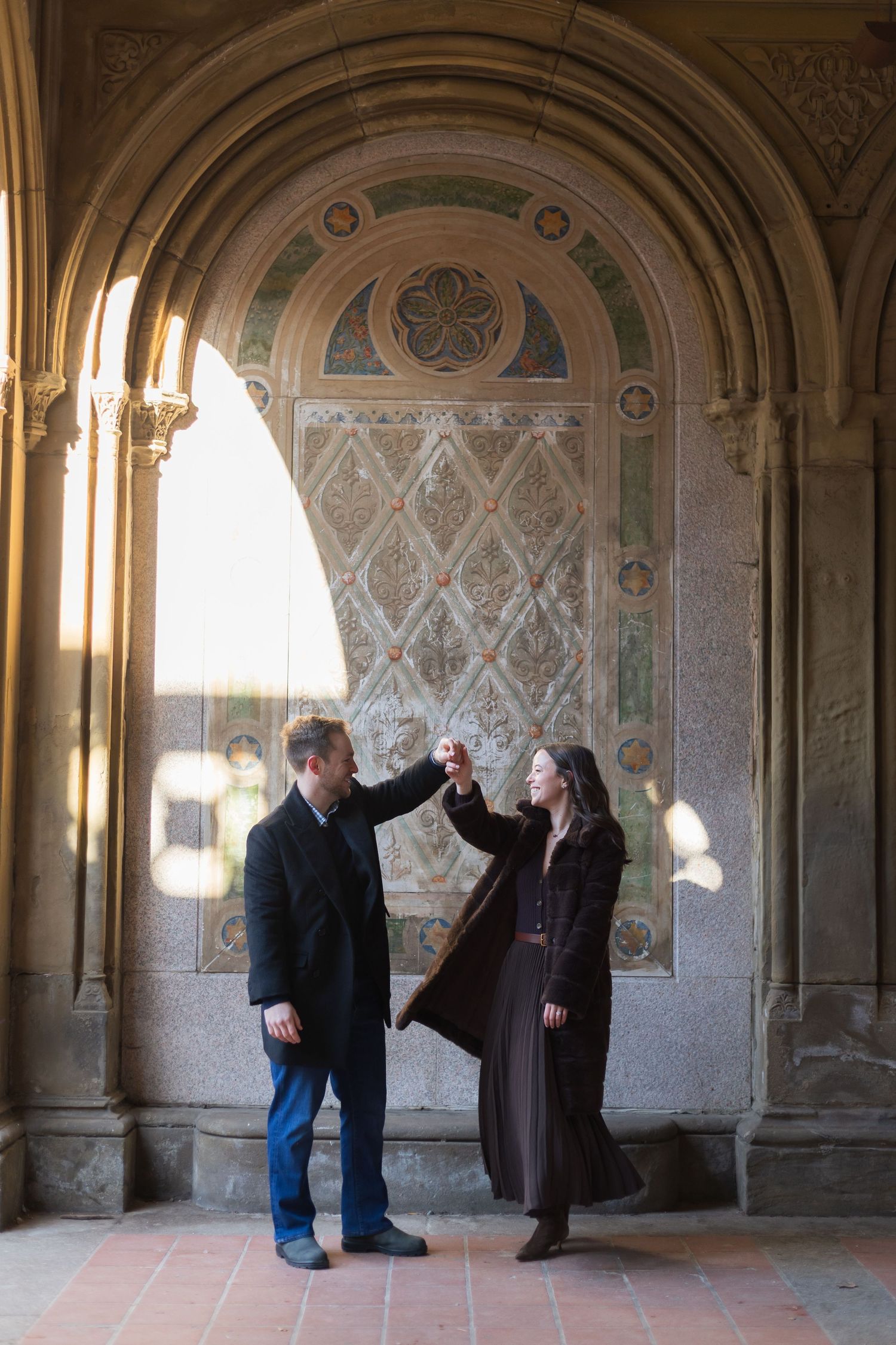 A man spinning his fiancee under one of the archways of Bethesda Terrace.