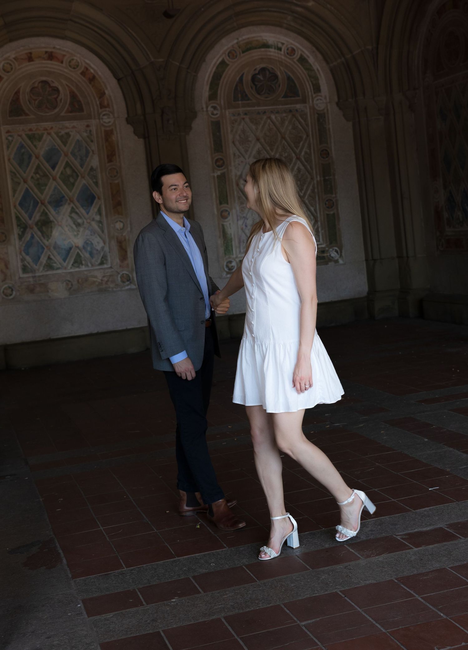 Couple in elegant attire sharing a romantic moment in an ornate architectural arcade with arched ceilings.