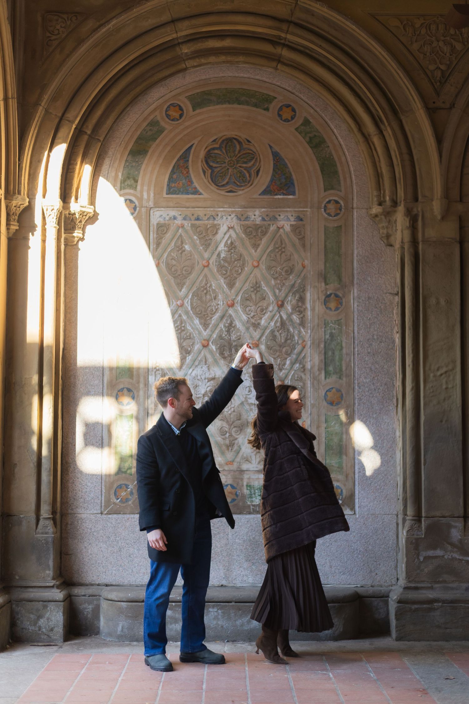 A man spinning his fiancee under one of the archways of Bethesda Terrace.