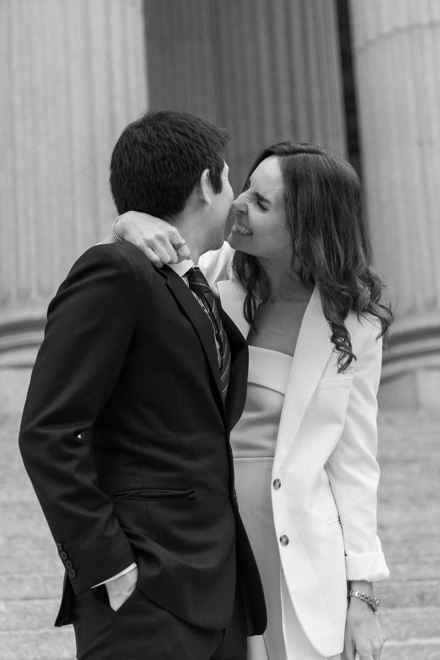 A romantic black and white wedding photo series showing a couple in formal attire sharing intimate moments against a column backdrop.