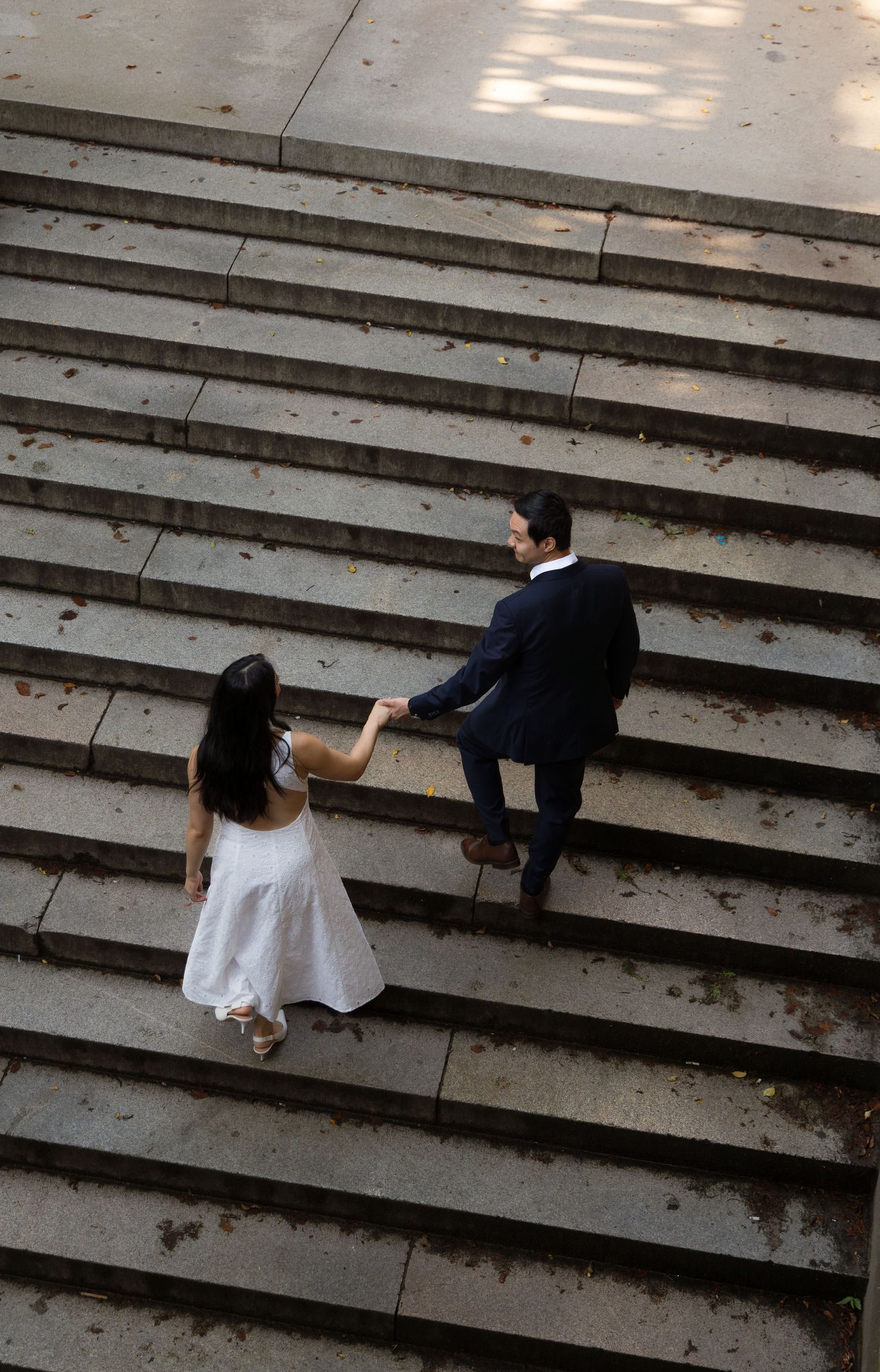 Aerial view of a couple in wedding attire holding hands while walking up concrete steps.