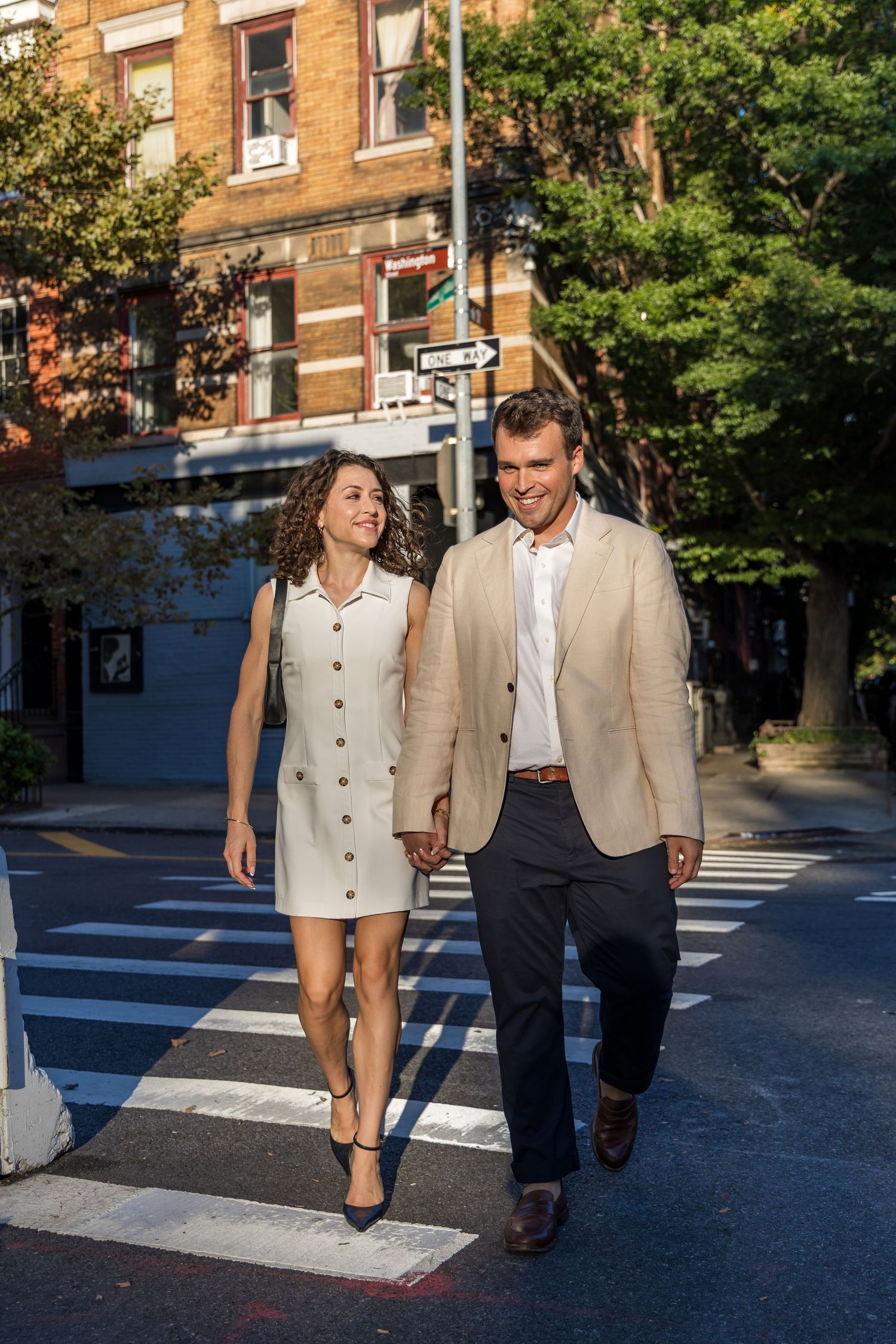 A couple holds hands while walking past historic red-brick townhouses on Bank Street in the West Village.