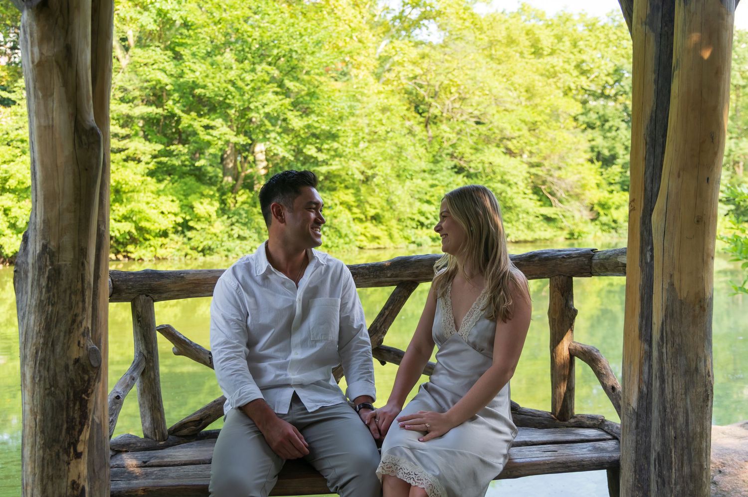 A couple sits together on a rustic wooden bench in a lush green park, smiling and enjoying each other's company.