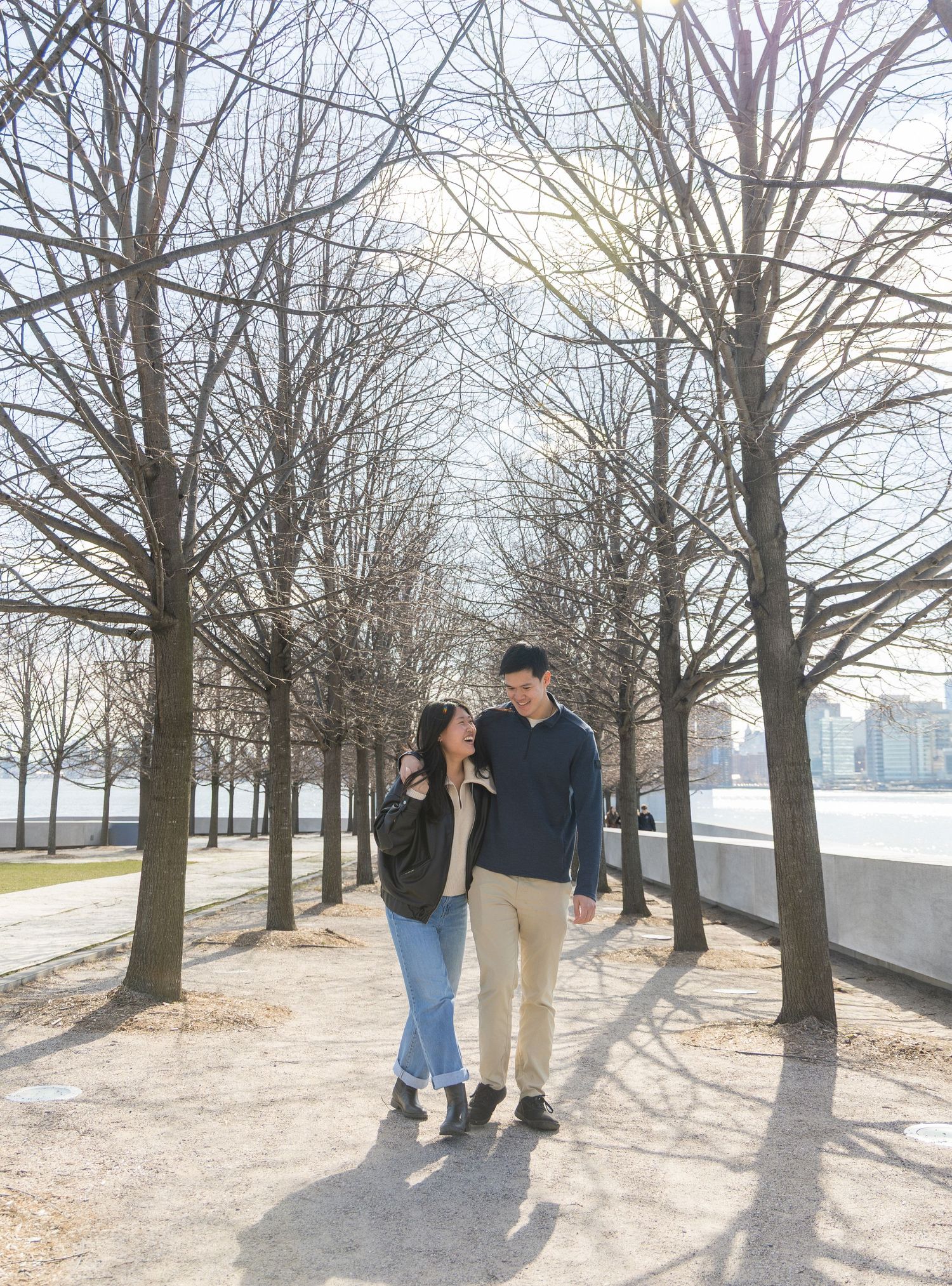 Couple walking hand in hand among bare winter trees on a sunny day outdoors.