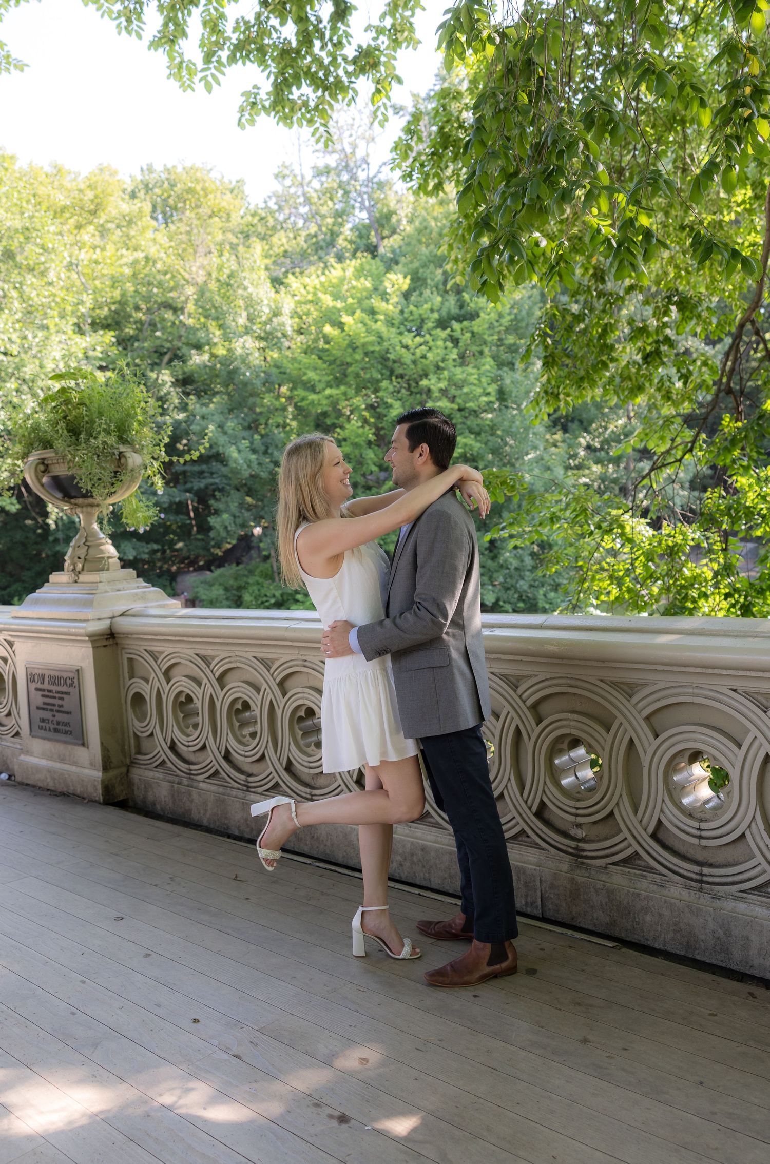 Couple embracing and dancing on Bethesda Terrace in Central Park, surrounded by lush green trees.