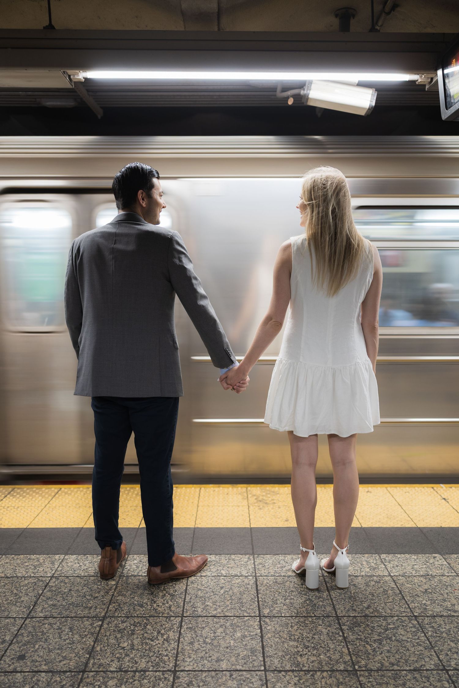 Couple holding hands on NYC subway platform watching a train pass by in motion blur.
