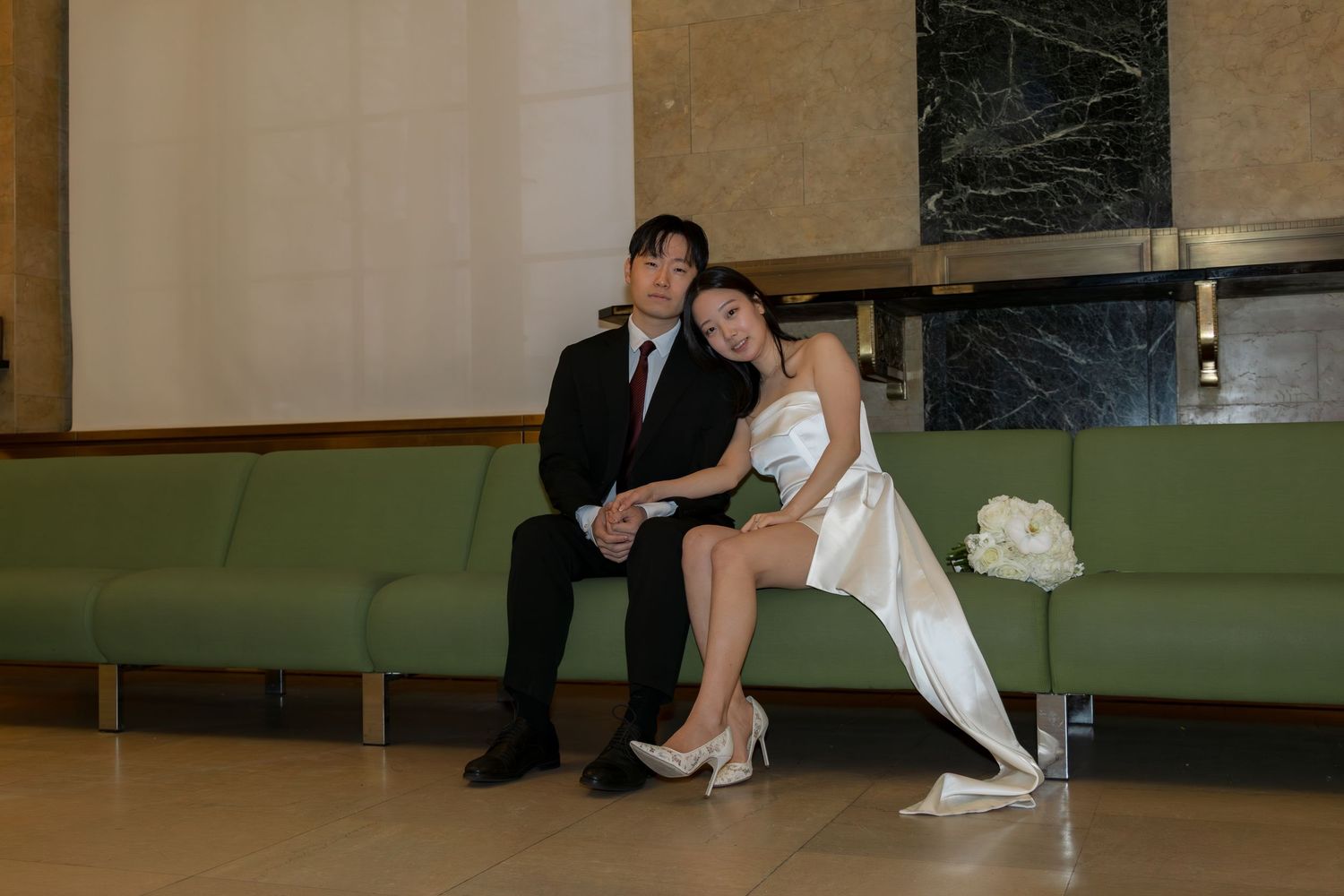 Bride and groom sitting on the iconic green couches inside the Manhattan Marriage Bureau waiting for their ticket number to be called