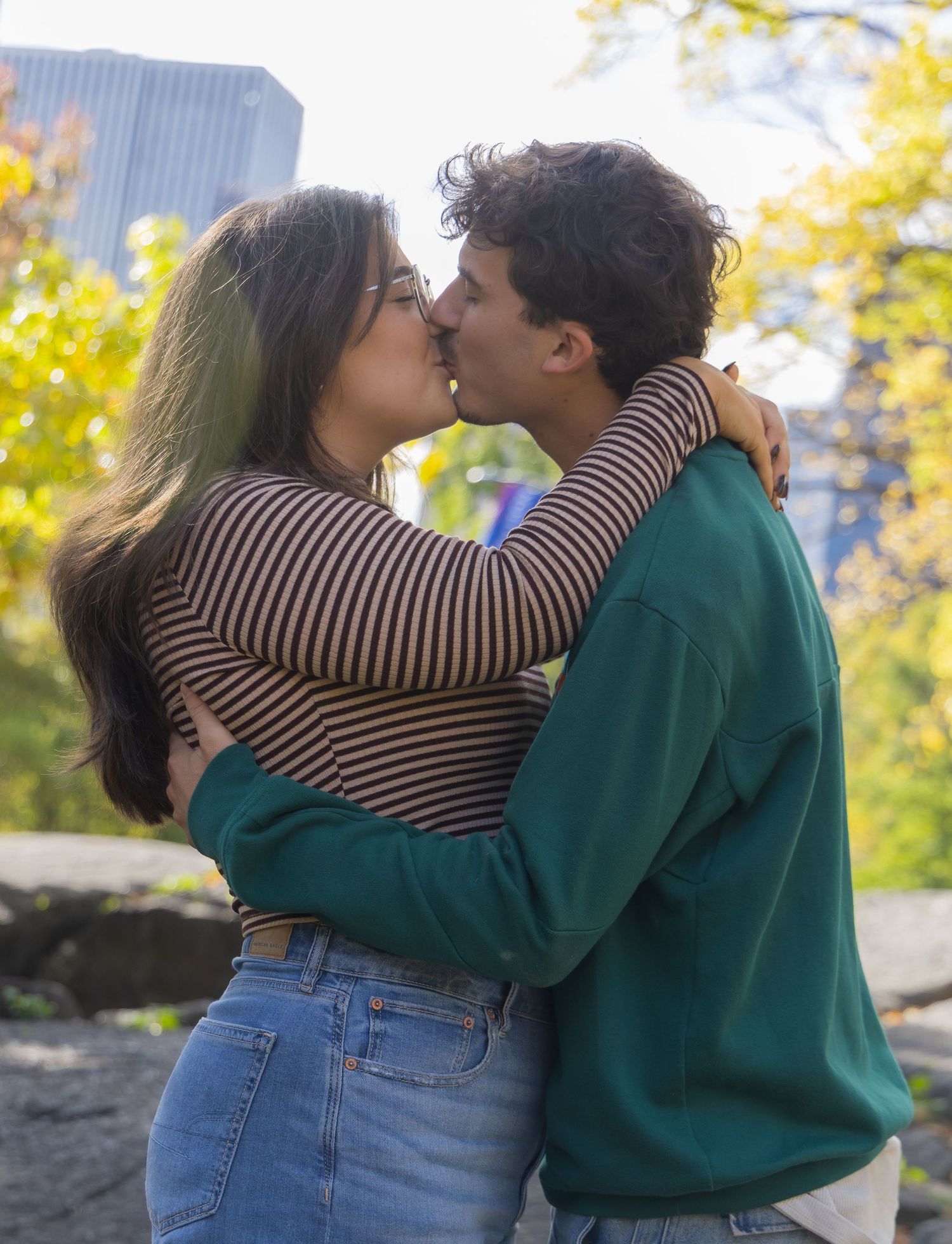 A couple in a striped shirt and green sweater share an intimate embrace outdoors during autumn in Central Park