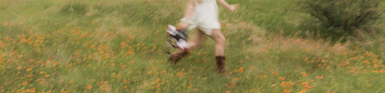 Blurred motion shot of a woman in a white dress running through an orange wildflower field.