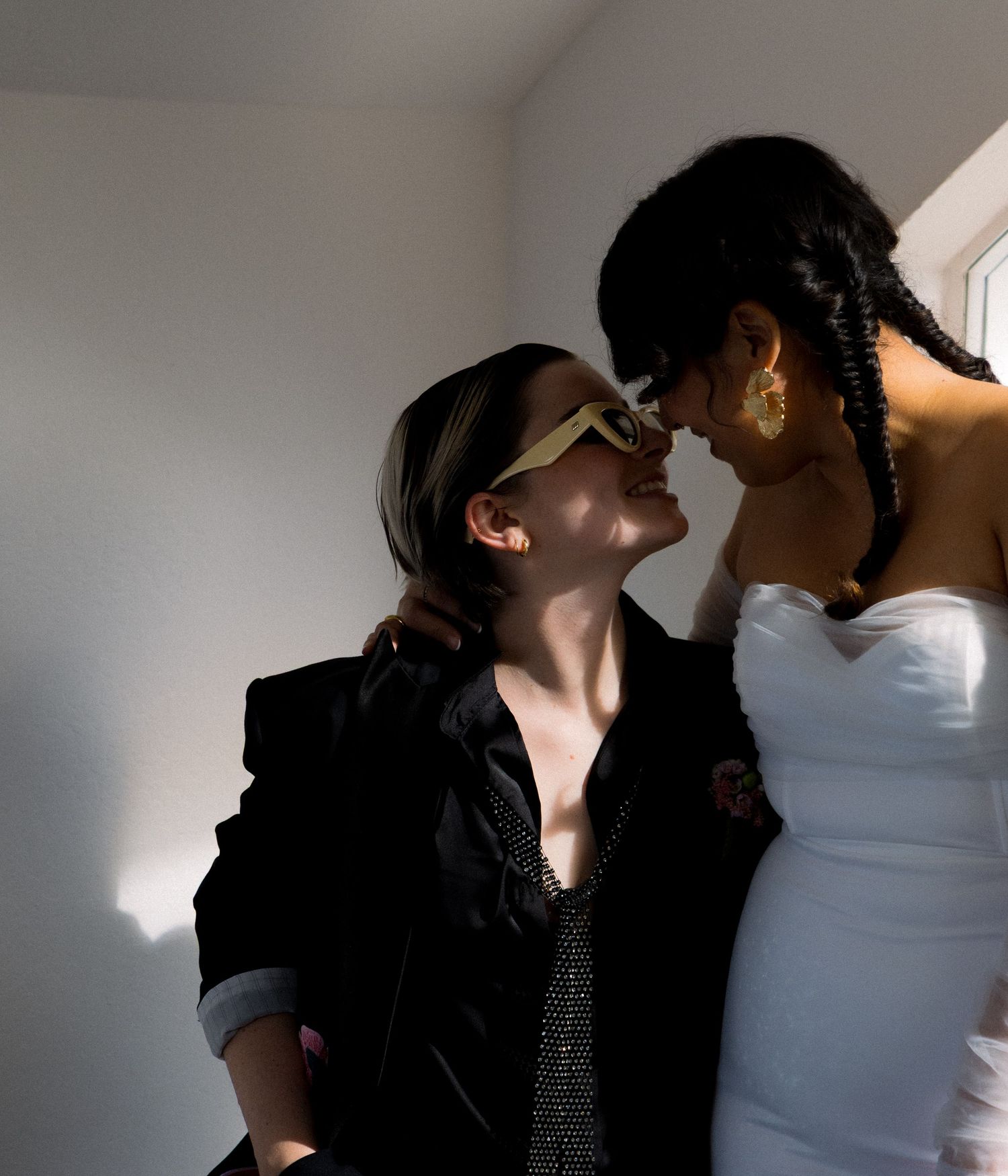 Two people in an intimate moment share a tender scene with dramatic lighting against a white wall.