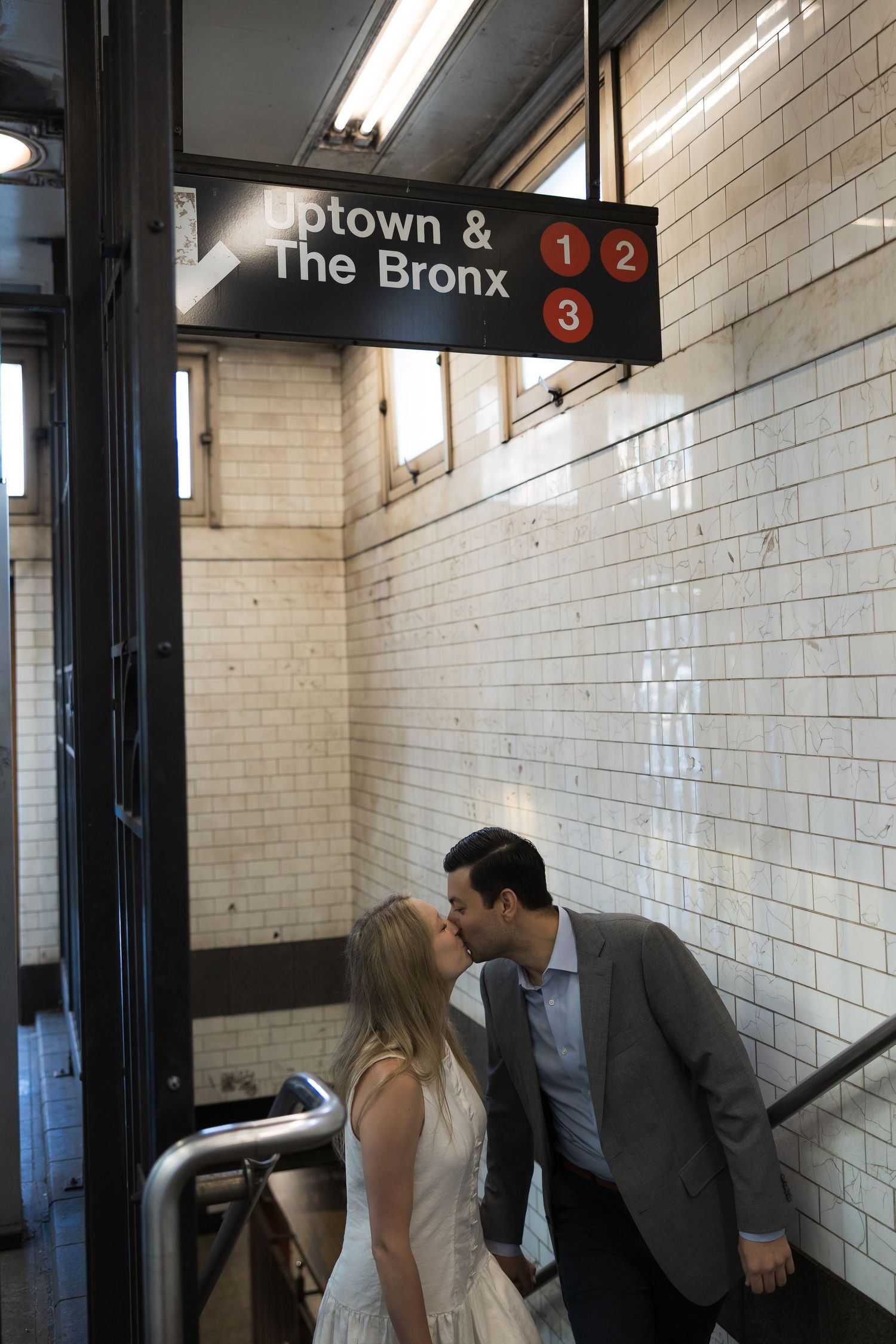 Couple sharing a romantic kiss under NYC subway sign for Uptown and The Bronx lines 1, 2, and 3.