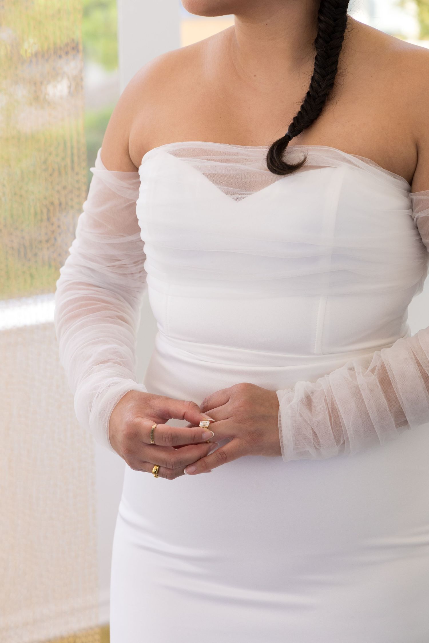 Close-up view of an elegant off-shoulder white wedding dress with sheer long sleeves in natural lighting.